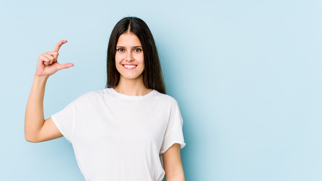 Mujer joven en azul sosteniendo algo poco con los dedos índices, sonriente y confiado.