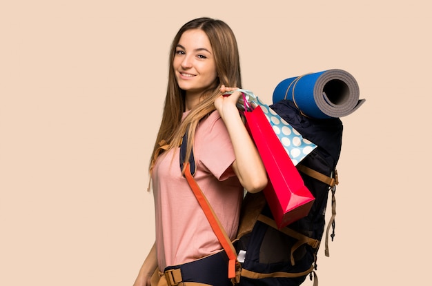 Mujer joven del backpacker que sostiene muchos bolsos de compras en fondo amarillo aislado