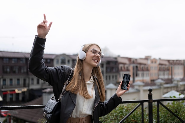 Mujer joven bailando con auriculares usando un teléfono móvil en el contexto de un panorama de la ciudad