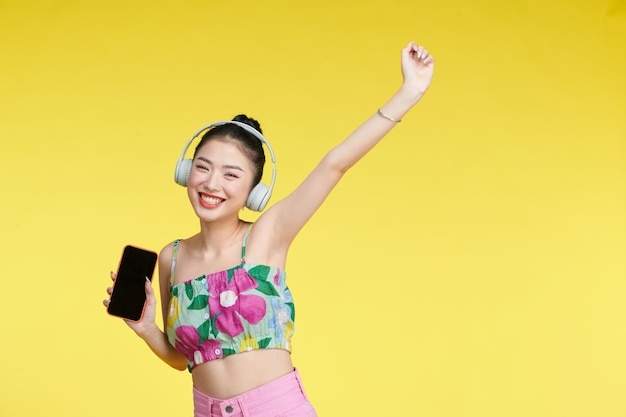 Mujer joven bailando mientras escucha música con auriculares y teléfono celular