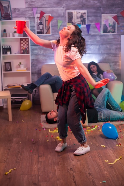 Mujer joven bailando sola en la fiesta de amigos. Grupo de amigo tirado en el suelo.