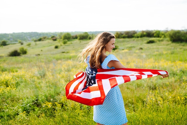 Mujer joven con la bandera americana de los E.E.U.U. en el prado floreciente Día de la Independencia el 4 de julio