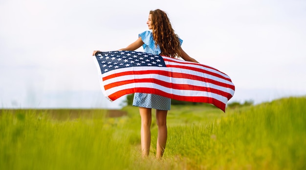 Mujer joven con la bandera americana de los E.E.U.U. en el prado floreciente Día de la Independencia el 4 de julio