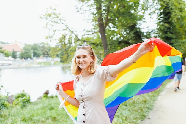 Mujer joven con la bandera del arco iris del orgullo LGBTQI en la calle en el concepto del Mes del Orgullo del parque