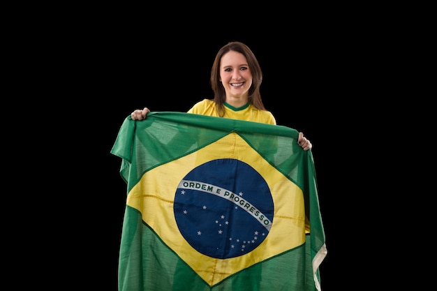 Mujer joven con bandera brasileña sobre una pared negra.