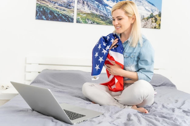 Mujer joven con bandera de Estados Unidos usando una computadora portátil, día de la independencia en línea.