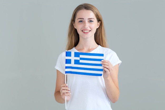 Foto mujer joven con la bandera de grecia en mano aislado en gris