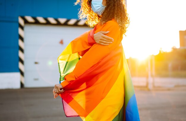 Mujer joven con bandera LGBT y máscara protectora