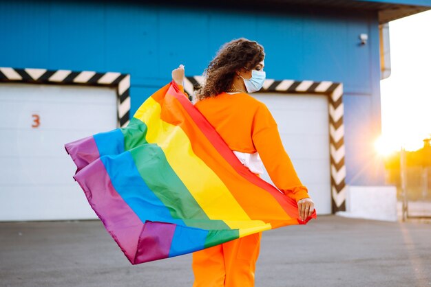 Mujer joven con bandera LGBT y máscara protectora