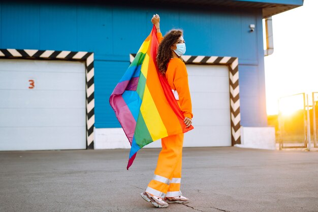 Mujer joven con bandera LGBT y máscara protectora