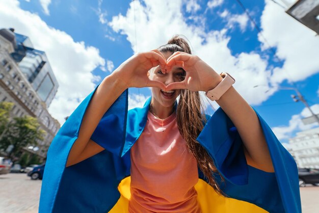 Mujer joven con bandera ucraniana muestra corazón con las manos