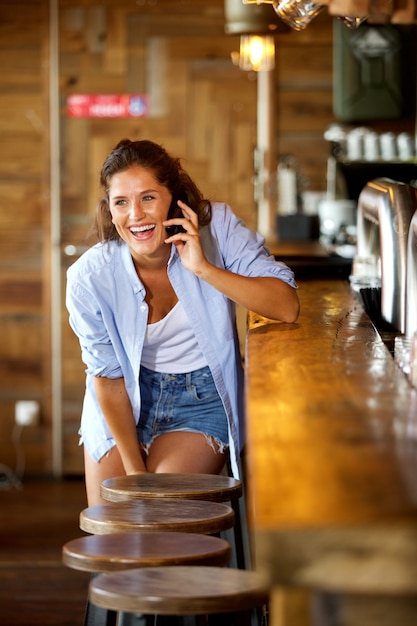 Mujer joven en el bar hablando por móvil riendo