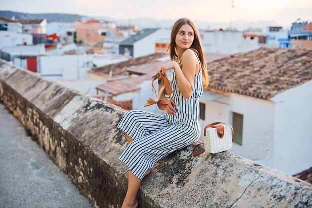 Mujer joven bastante elegante con elegantes sandalias en manos posando en la calle.