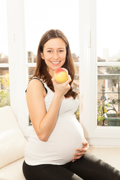 Mujer joven bastante feliz embarazada comiendo una manzana