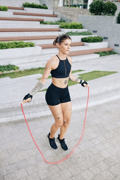 Mujer joven bastante en forma saltando con saltar la cuerda al aire libre para calentar antes de entrenar