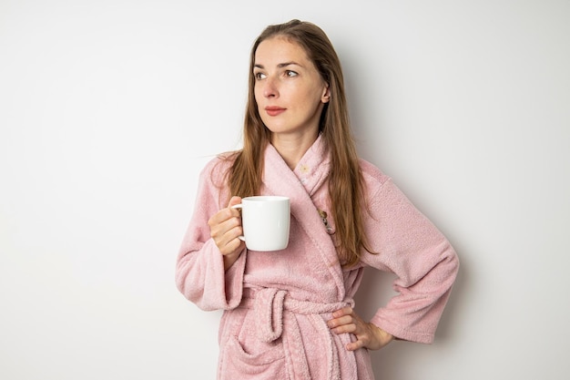 Mujer joven en una bata de baño bebe café sobre un fondo blanco.