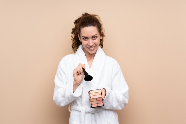 Mujer joven en una bata de baño con paleta de maquillaje sobre aislado