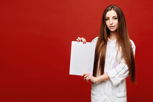 Mujer joven en una bata blanca con una hoja de papel blanca vacía en sus manos. Copie espacio para su texto. Concepto de salud y medicina