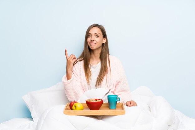 Mujer joven en bata con desayuno señalando con el dedo índice una gran idea