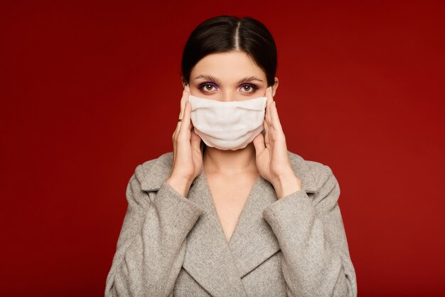 Mujer joven en bata gris y máscara médica posando