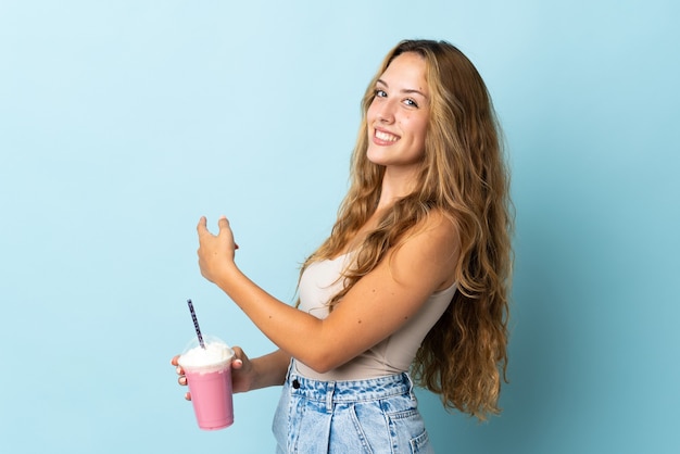 Mujer joven con batido de fresa aislado apuntando hacia atrás