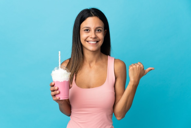 Mujer joven con batido de fresa apuntando hacia el lado para presentar un producto