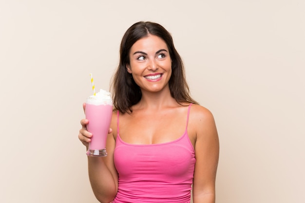 Mujer joven con batido de fresa mirando hacia arriba mientras sonríe