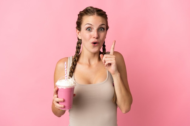 Mujer joven con batido de fresa en rosa con la intención de darse cuenta de la solución mientras levanta un dedo