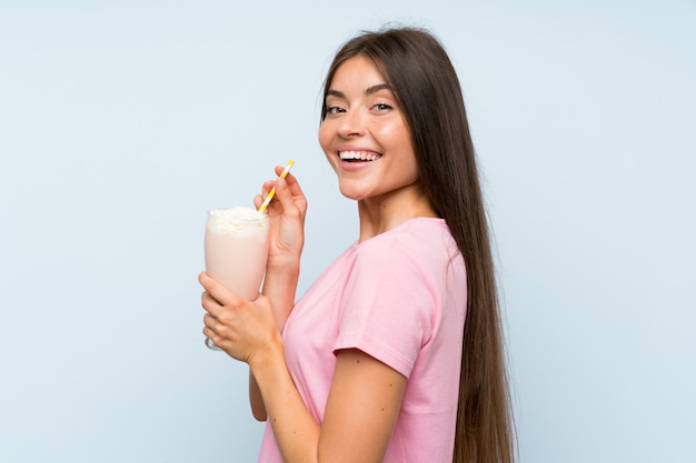 Mujer joven con batido de fresa sobre pared azul aislado