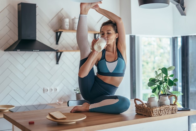 Mujer joven bebe leche y hace un ejercicio de estiramiento.