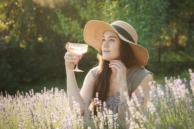 Mujer joven bebe vino en el campo de lavanda al atardecer