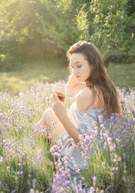 Mujer joven bebe vino en el campo de lavanda al atardecer