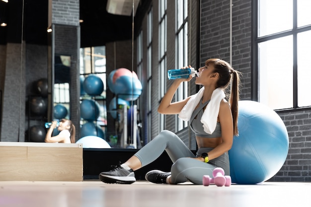 Mujer joven bebida asiática agua después de entrenamiento en una habitación