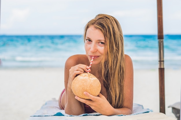 Mujer joven, bebida, leche de coco, en, chaiselongue, en, playa