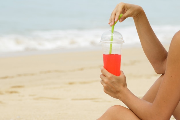 Mujer joven con una bebida refrescante roja en la playa