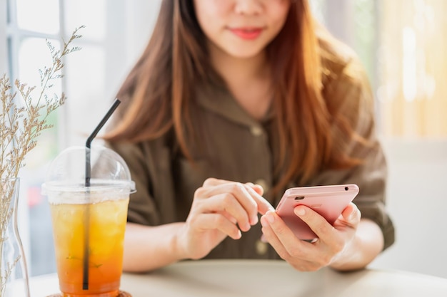 Mujer joven con bebidas mediante teléfono móvil y relajarse en la cafetería, estilo de vida moderno