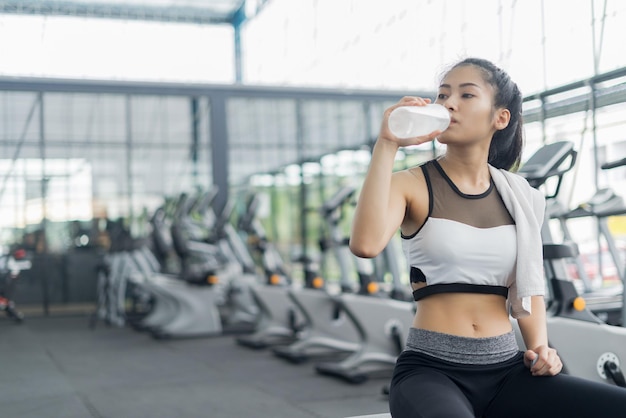 Mujer joven bebiendo agua de botella mientras está sentada en el gimnasio