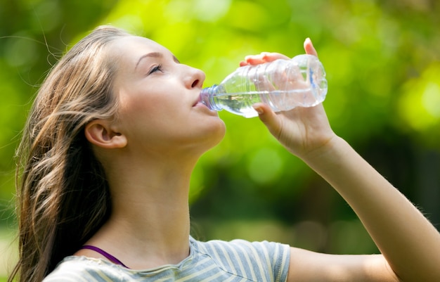 Mujer joven bebiendo agua de botella de plástico