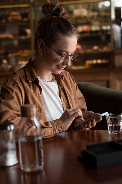 Mujer joven bebiendo agua en la cafetería espera comida ordenada mediante teléfono móvil