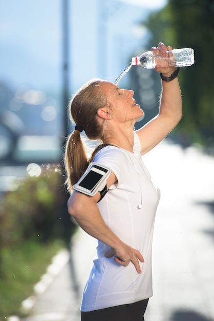 mujer joven bebiendo agua después de la mañana trotar entrenamiento ciudad amanecer en segundo plano.