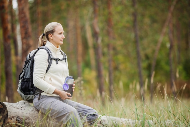 Foto mujer joven bebiendo agua con mochila en el valle del bosque