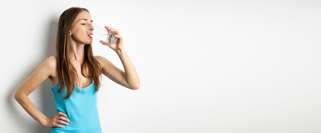 Mujer joven bebiendo agua de un vaso sobre un fondo blanco Banner