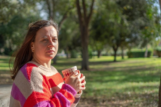 Mujer joven bebiendo una bebida caliente en la naturaleza