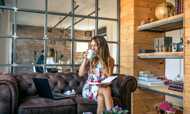 Foto mujer joven bebiendo café mientras está sentada en el sofá en la oficina