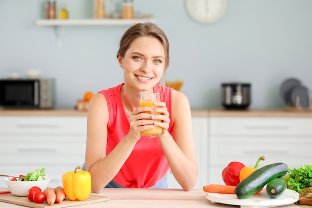 Mujer joven bebiendo jugo saludable en la cocina. Concepto de dieta