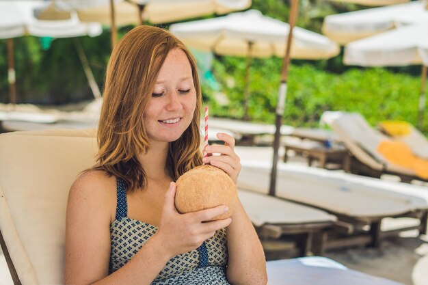 Mujer joven bebiendo leche de coco en Chaise-longue en la playa. Dream scape Escape con belleza. Los beneficios del agua de coco.