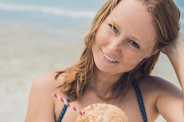 Mujer joven bebiendo leche de coco en la playa