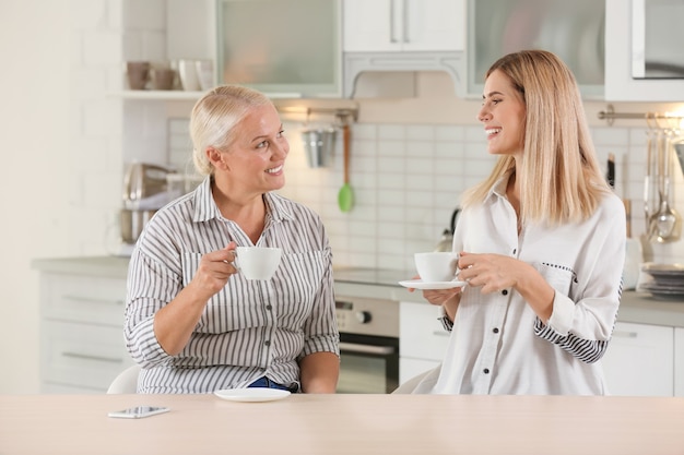 Mujer joven bebiendo té con la anciana madre en casa