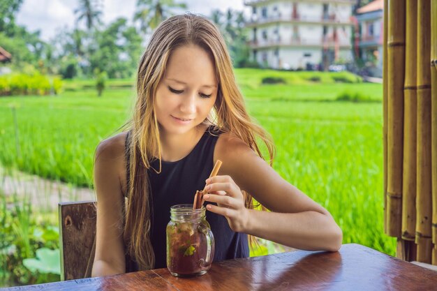 Mujer joven bebiendo té frío con canela en campo de arroz