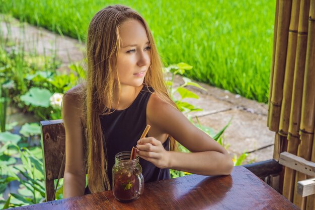 Mujer joven bebiendo té frío con canela en campo de arroz